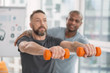 © zinkevych - Sports equipment. Selective focus of orange dumbbells being held by a nice pleasant man