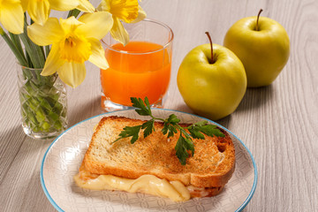 Toast with butter and cheese on white plate, two apples, glass of orange juice and bouquet of spring flowers