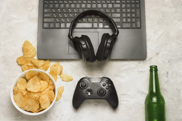 Wall Mural - Laptop, Gamepad, Headphones, Potato chips, Bottle of Beer on a light stone background. Concept of computer games and leisure