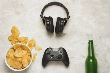 Wall Mural - Concept of computer games. Gamepad, Headphones, Potato chips, Botle of Beer on a light stone background