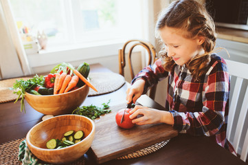 child girl helps mom to cook and cut fresh vegetables for salad with knife. Kids learning house work on farm on summer vacations