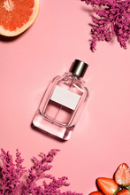 Top View Of Bottle Of Perfume With Pink Flowers, Orange And Strawberry On Pink Surface