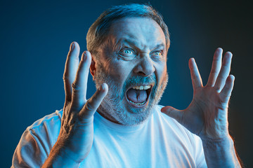 the senior emotional angry man screaming on blue studio background