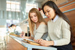 © Seventyfour - Two beautiful girls studying notes sitting at desk in lecture hall of modern college, copy space