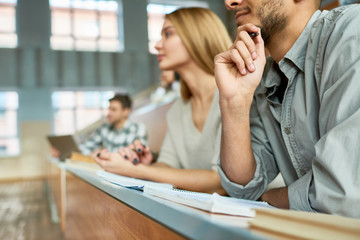 multi-ethnic group of students sitting at desk in lecture hall of modern college and listening to pr