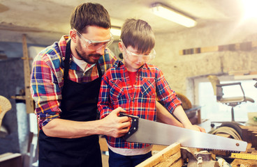 Wall Mural - family, carpentry, woodwork and people concept - father and little son with saw sawing wood plank at workshop