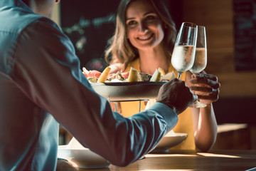 Happy young couple in love toasting with champagne during romantic dinner with seafood as oysters and crabs at the restaurant