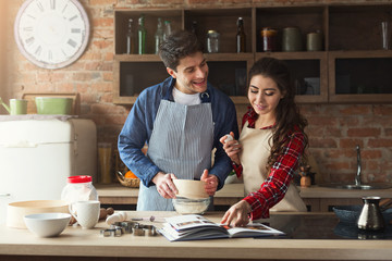 Happy young woman and man baking in loft kitchen