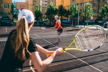 two women playing tennis outdoor. Practicing tennis on the tennis court at sunny day, on a city background