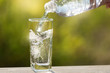 in a tall glass pouring water from a bottle, in the open space, sunlight and bokeh