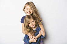 Joyful Beautiful Child With Her Sister Close To A White Wall