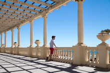 Fashionable Young Man Standing Near Balustrade Of Pergola With Columns Overlooking Ocean