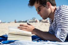 Young Man Reading Paper Book On The Beach