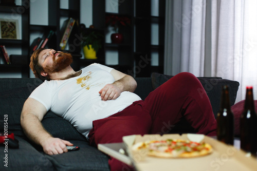 Ugly fat man sleeps on the couch after eating pizza and playing video-games