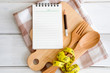 Notepad on chopping board with a wooden fork and spoon and measuring tape on white table , recipes food or diet plan for healthy habits shot note background concept