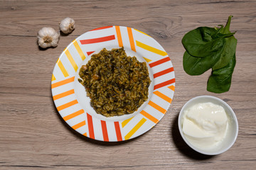 Delicious homemade risotto with spinach, onion and carrots. Decorated with yoghurt and garlic. On a wooden background.