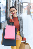Fototapeta Pomosty - attractive woman standing on street with shopping bags and talking by smartphone