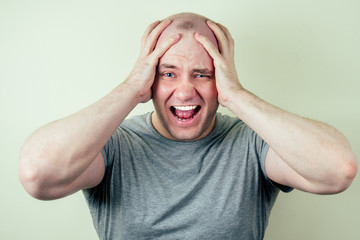 a portrait of a bald man is sad against a gray background. problem of male pattern baldness. sadness, vexation and anger