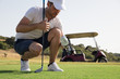 © StudioWout - Golf player putting ball on the course before teeing off in front of golf cart
