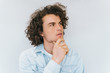 © iuricazac - Studio shot of handsome pensive male model with curly hair, wears blue shirt, looking up thinking about problem, holding his chin on white. People, business concept. Copy space for your advertisement