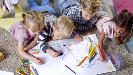 high angle view of group of four primary school children lying on the floor and drawing beautiful pi