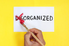 Disorganized Is Organized Concept. Hand With Brush. Corrected Word Disorganized On Yellow Background.