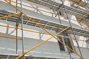 scaffolding near a new house, building exterior, construction and repair industry, white wall and window, yellow pipe