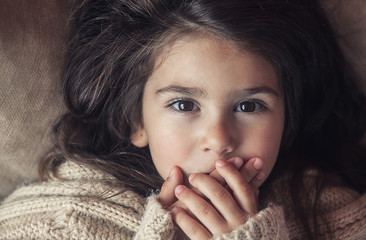 little beautiful child  girl with big brown eyes lies and closes her mouth with her hands in silence