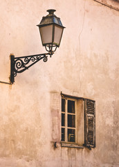 Old street lamp on forged handle and window with one shutter on faded wall of house in Nice, Cote d'Azur, France