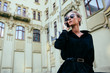 © Maksym Azovtsev - Gorgeous young lady in elegant black coat communicating by cell phone, wearing sunglasses, standing near the old building. Outside.