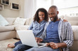 © Monkey Business - Young black couple using laptop sitting on the floor at home