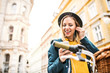 © Halfpoint - Young woman with bicycle and smartphone in sunny spring town.