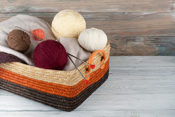 Wall Mural - Ball of wool, needles and woolen sweater with spokes for handmade knitting in basket on wooden table.