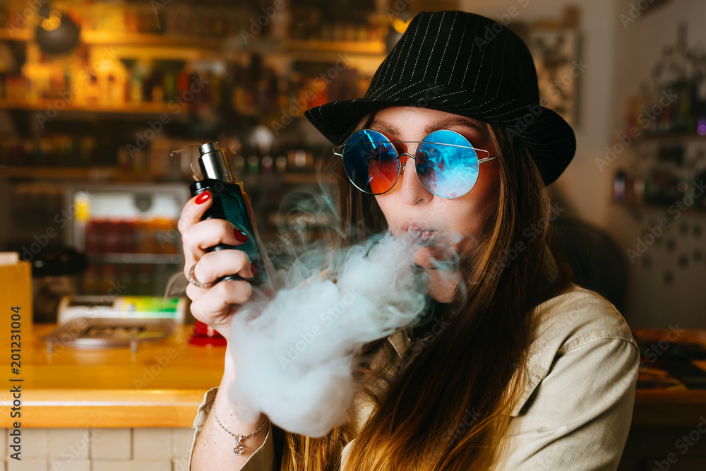 Vaping girl. Young hipster woman vape e-cig at the vapeshop. Hip-hop style.  Closeup. Stock Photo