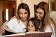 © nagaets - Happy loving family. Pretty young mother and her sister reading a book to her daughter.