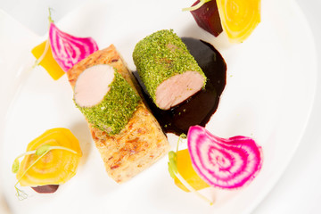 Roast pork tenderloin with crispy potato bread, marinated beetroots and green pepper sauce on a plate on a white background