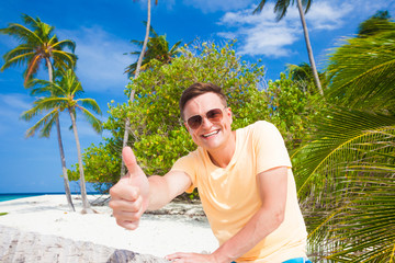 Wall Mural - picture of a young man in sunglasses showing thump up at tropical beach