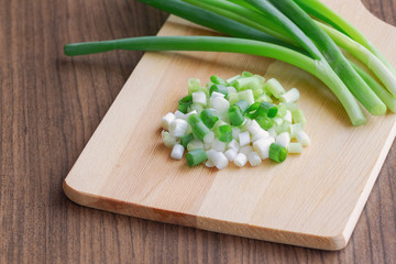 Wall Mural - Chopped fresh spring onion and knife put on wood cutting board on wooden table with copy space in top view. Prepare scallions for cooking. Food and vegetable concept for background or wallpaper.