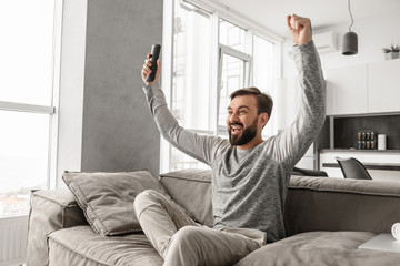 Wall Mural - Portrait of an excited young man holding TV remote control