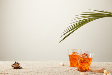 Wall Mural - close up view of cocktails with ice with fern and seashells on sand on grey background