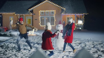 Wall Mural - Happy Young Father, Mother and Cute Little Daughter Play in Snowballs, Running around the Snowman They've Build in the Backyard of Their Idyllic House Decorated with Garlands. 