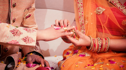 indian bride putting a wedding engagement ring on finger of groom.