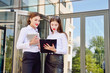 © salomonus_ - Business lady. Office staff. Two young girls with electronic tablets communicate against the background of a multi-storey glass office building. Electronic Gadget