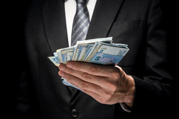 Wall Mural - Close up of man in black suit holding a lot of cash on black background