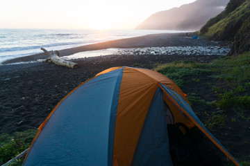 Wall Mural - Backpacking tent sits on the black sand of the Lost Coast backpacking trail in California at sunset