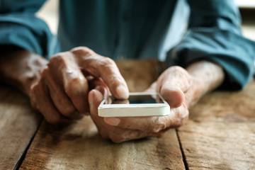 hands of old man working with digital smartphone in wood table
