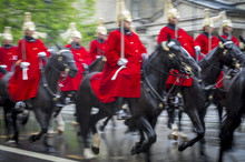 Royal Guards On Horseback Dressed In Ceremonial Red Coats Pass With Motion Blur In A Parade On A Rainy Day In London, England, UK. Shot With Slow Shutter Speed.