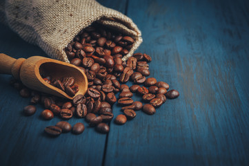 Fried coffee beans in a sackbag and wooden spoon on a blue textured background with copy space. Minimalist design for advertising in a cafe, top view.