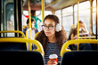 © dusanpetkovic1 - A cute beautiful young woman with curly hair is sitting in the bus seat listening to music drinking coffee and looking out of the window.
