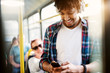 © dusanpetkovic1 - A young joyful man is smiling as he uses his phone and listens to music while traveling by bus.